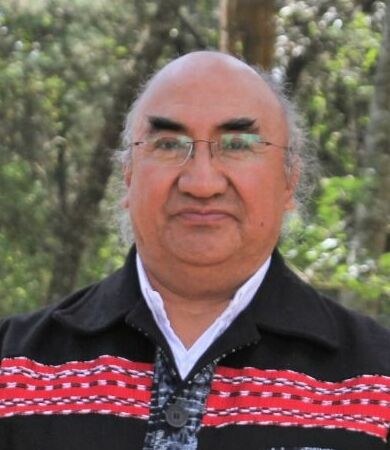 A portrait of a man with glasses wearing a woven red and black jacket
