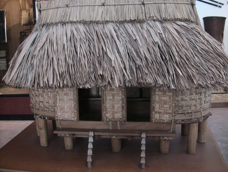 A model of a communal house with a steep thatched roof and carved gable