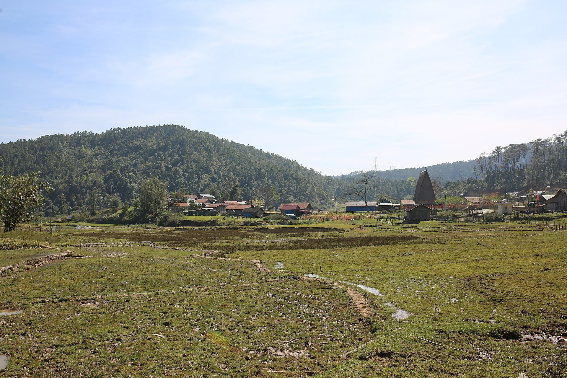 A wide valley of harvested fields with a village at the far edge and forested hills behind
