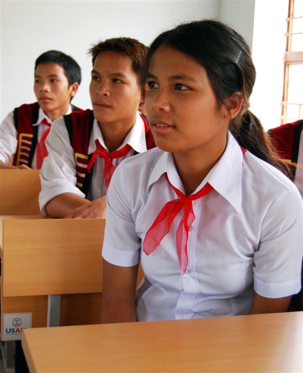 Three teenage students in white shirts and red neckerchiefs sitting at desks