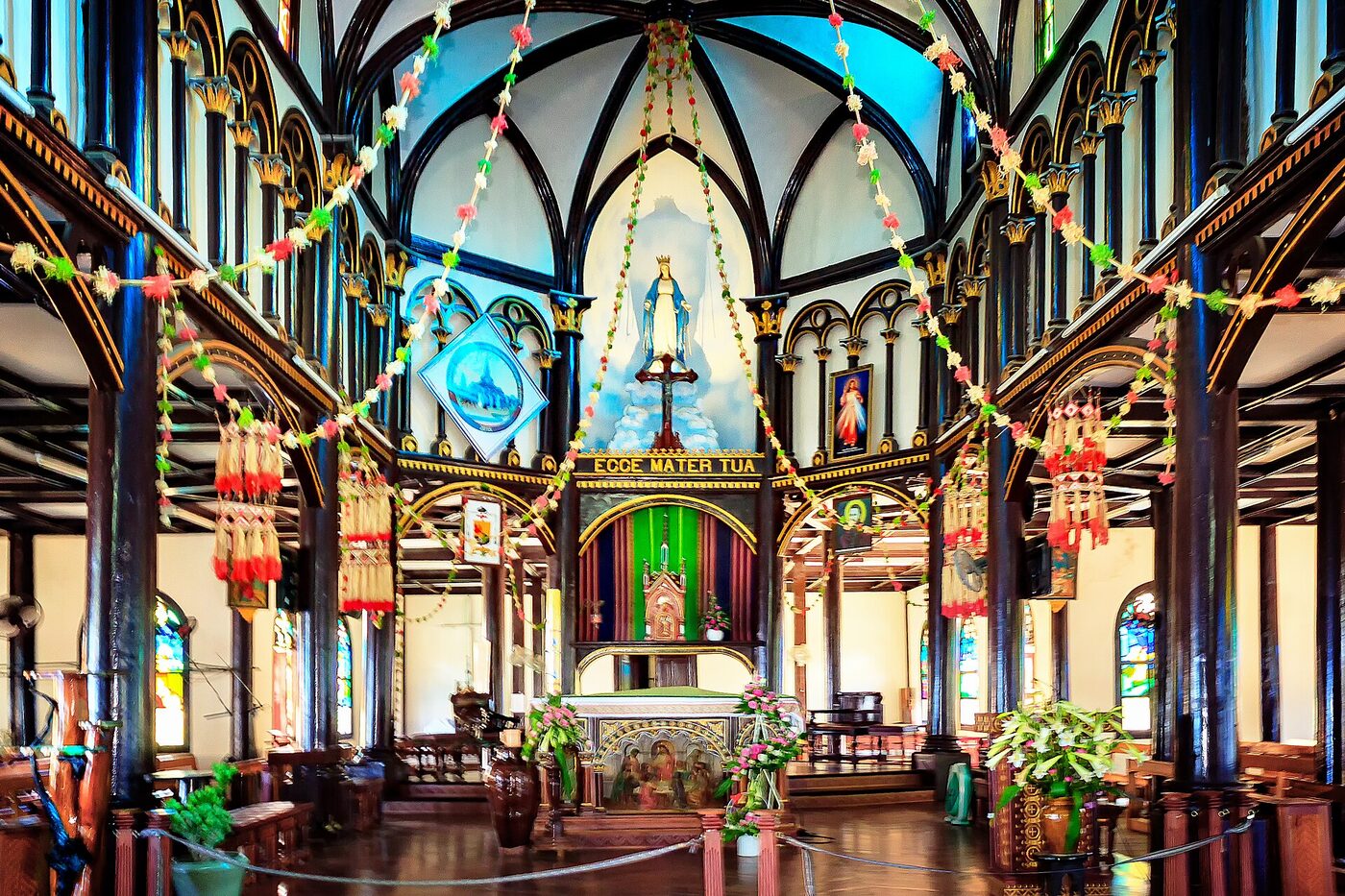 The wooden interior of a church, with rows of pews and carved timber columns