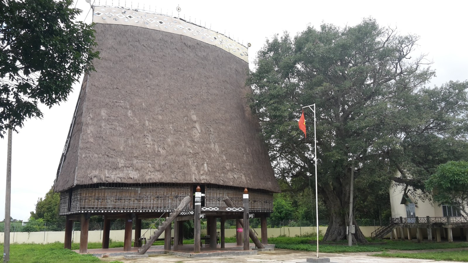 A tall communal house with a steep thatched roof rising to a point