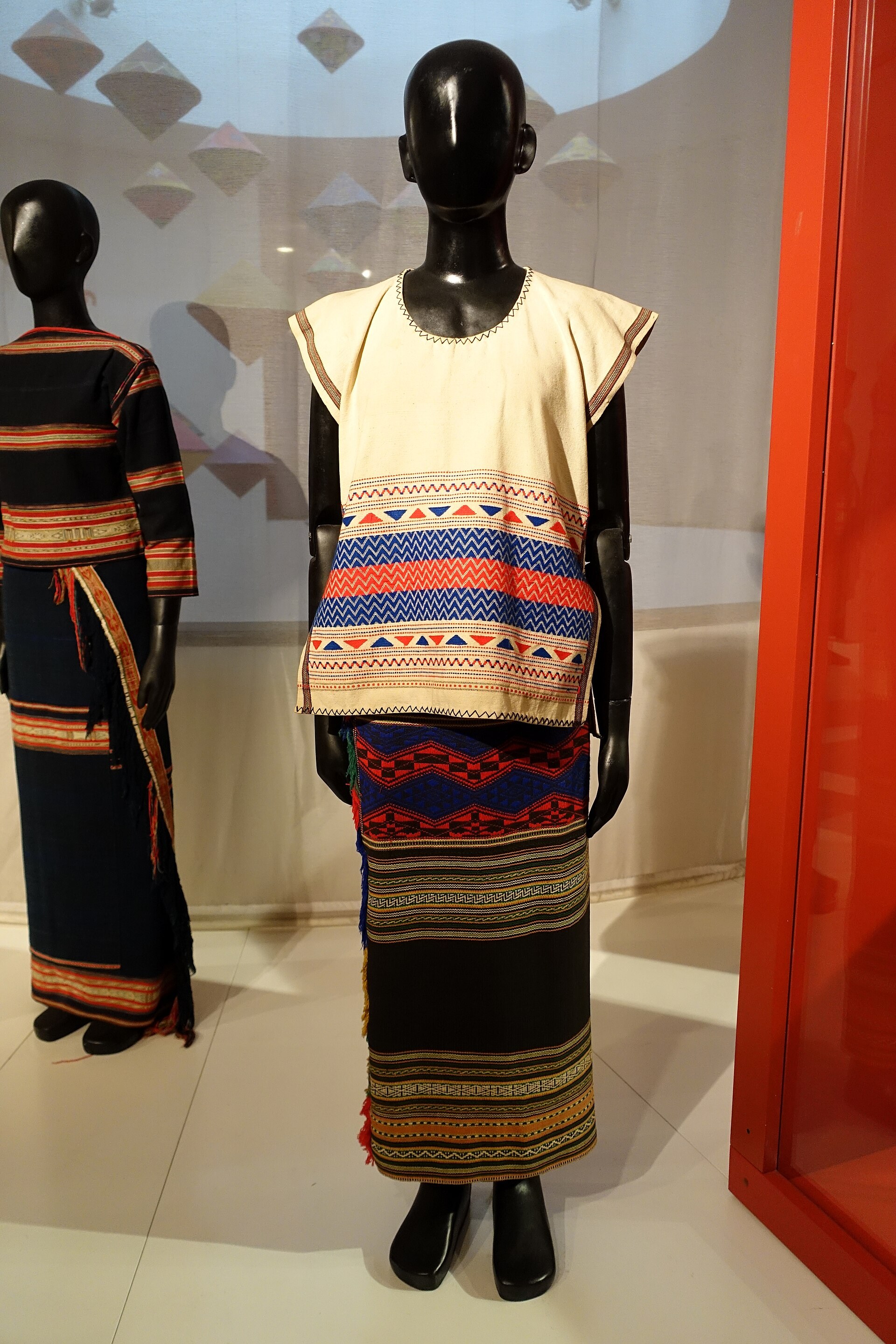 A Maa woman’s costume with broad bands of red and white on indigo, on a museum figure