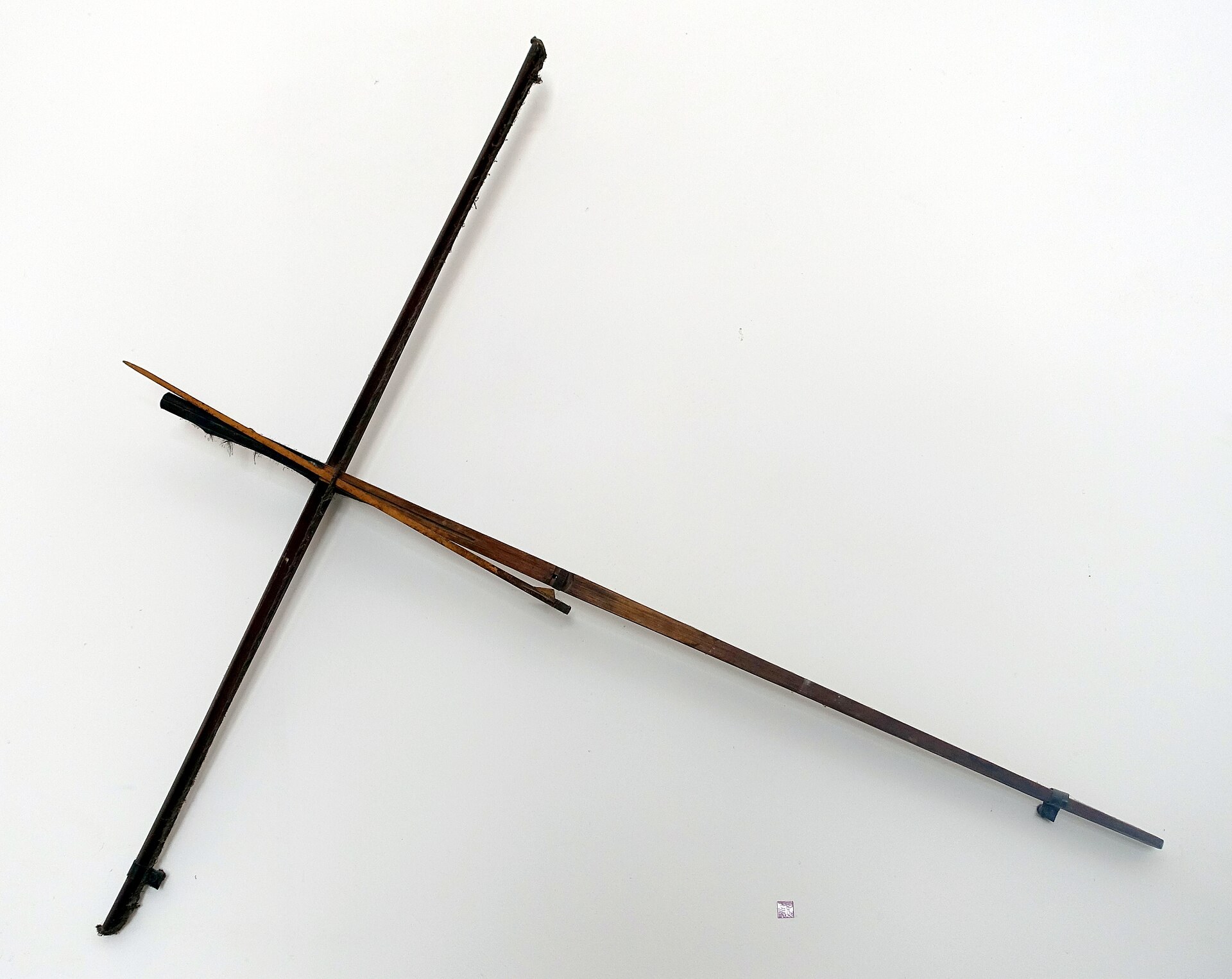 A large wooden crossbow with a wide bamboo bow, on a museum wall