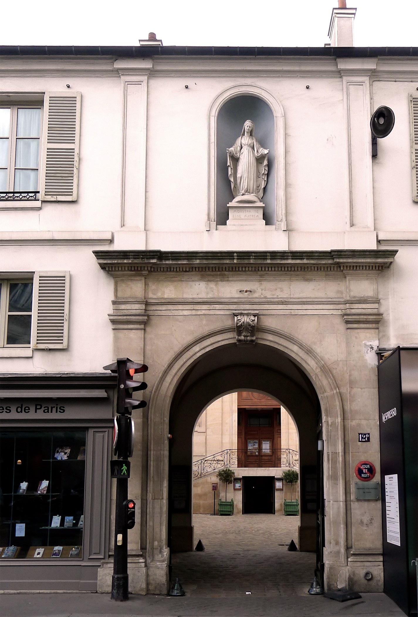 An arched stone gateway in a Paris street, with a statue in a niche above it
