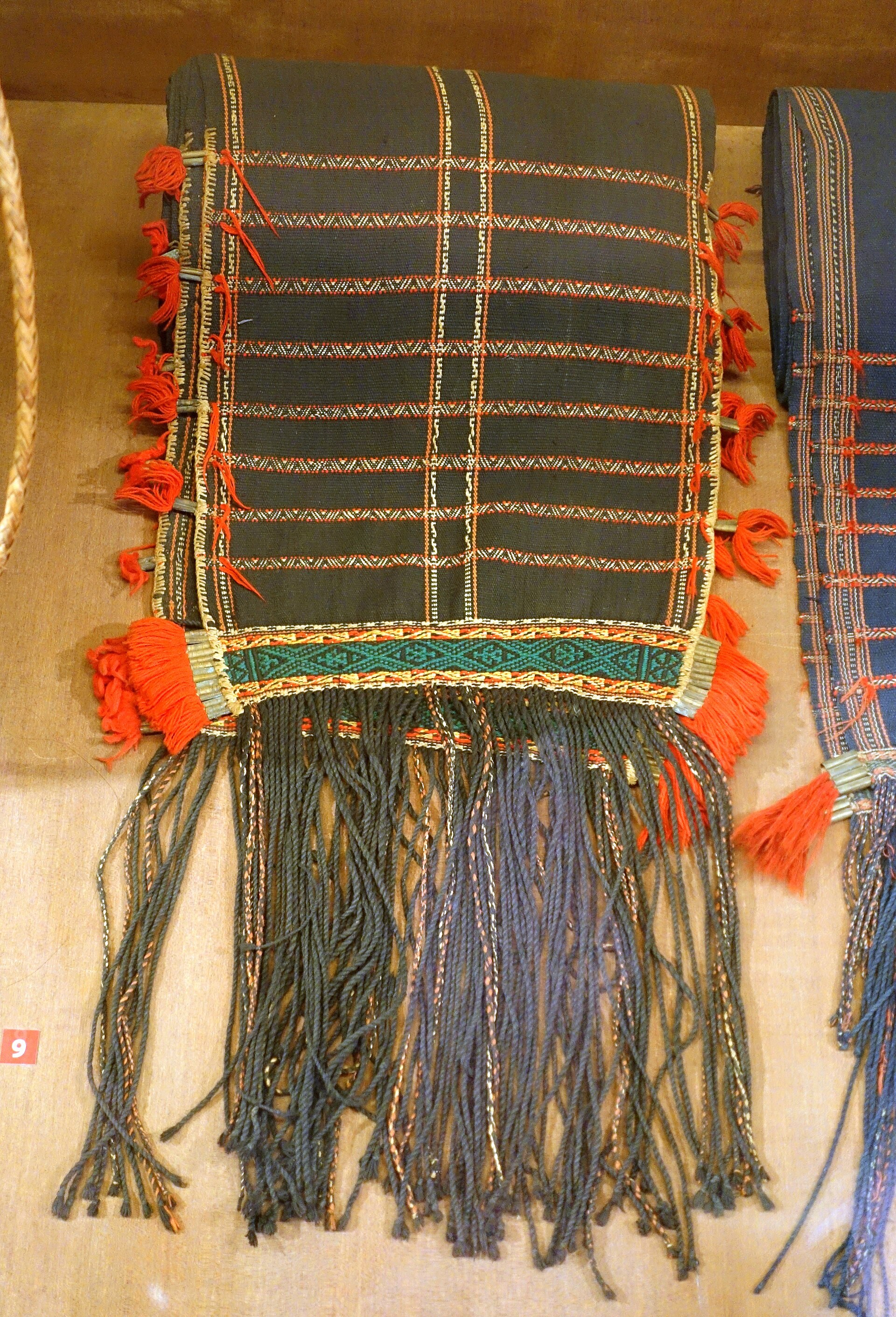 A long Mnong man’s loincloth with patterned ends, hung full length on a museum wall