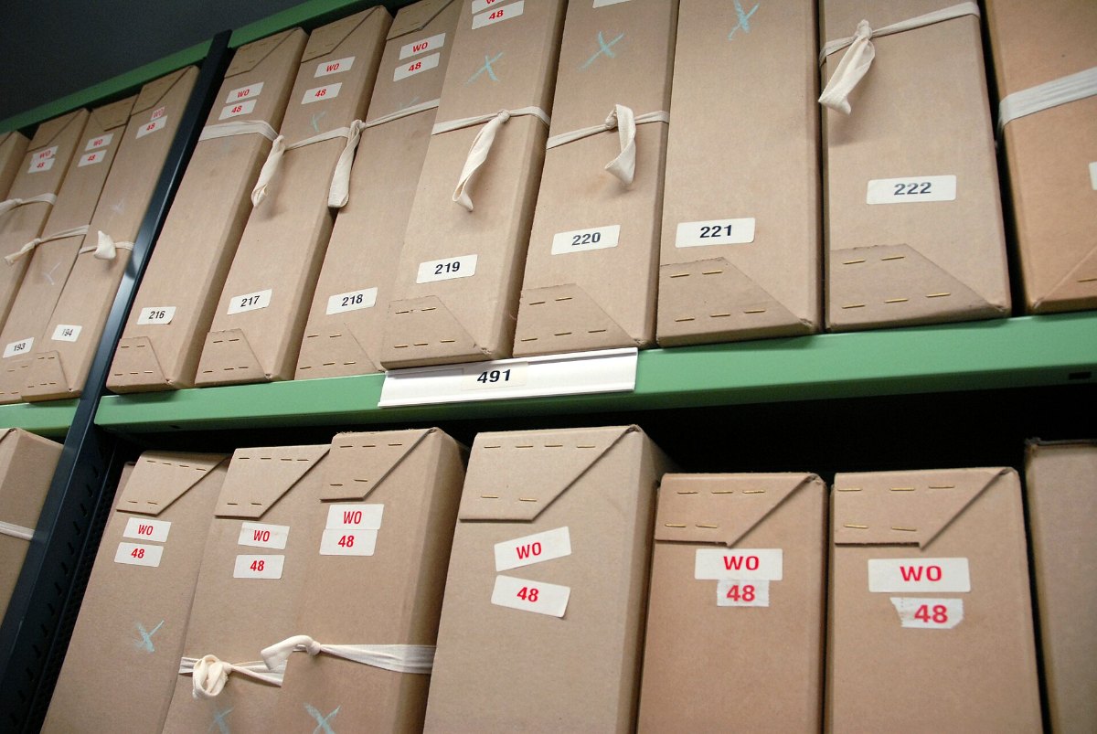 Brown archive boxes with labels standing in rows on metal shelving in a record store