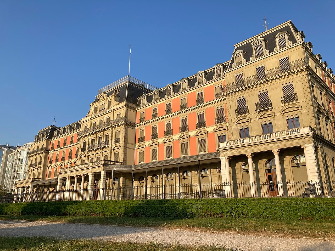 A long nineteenth-century building with a mansard roof beside a lawn