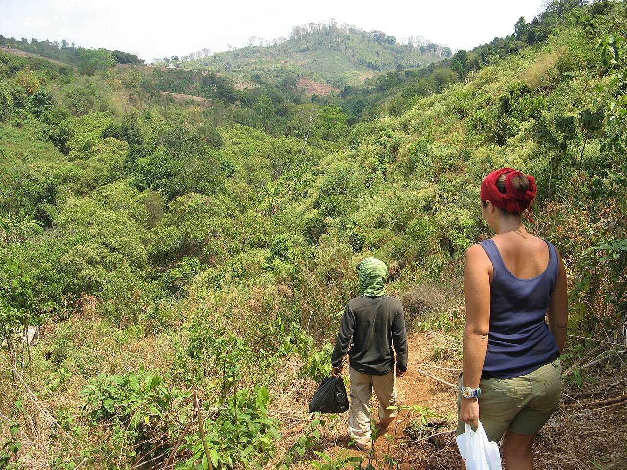 Two people walking up a narrow path into forested hills