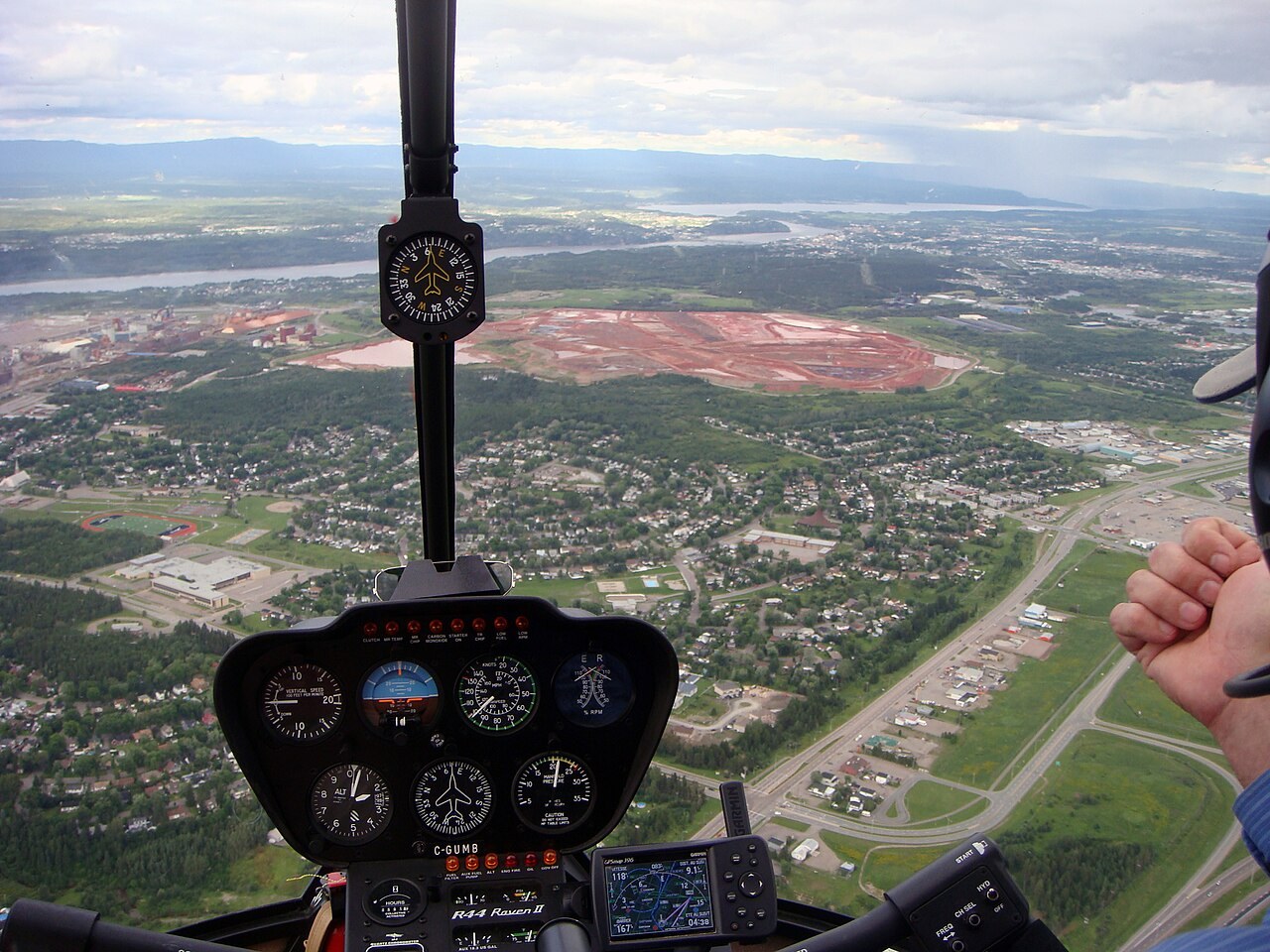 An aerial view through a helicopter windshield of a large rust-red basin beside a town and a river