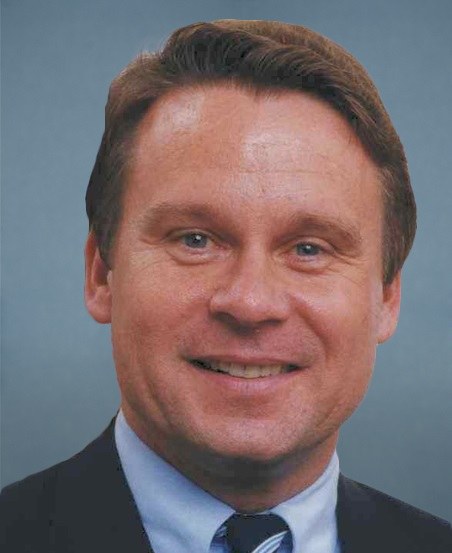 An official portrait of a smiling man in a suit and tie