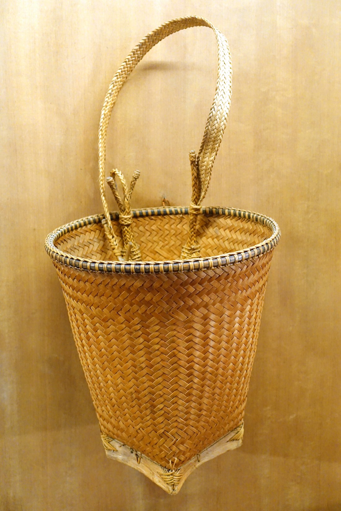 A tall woven basket with a belt strap