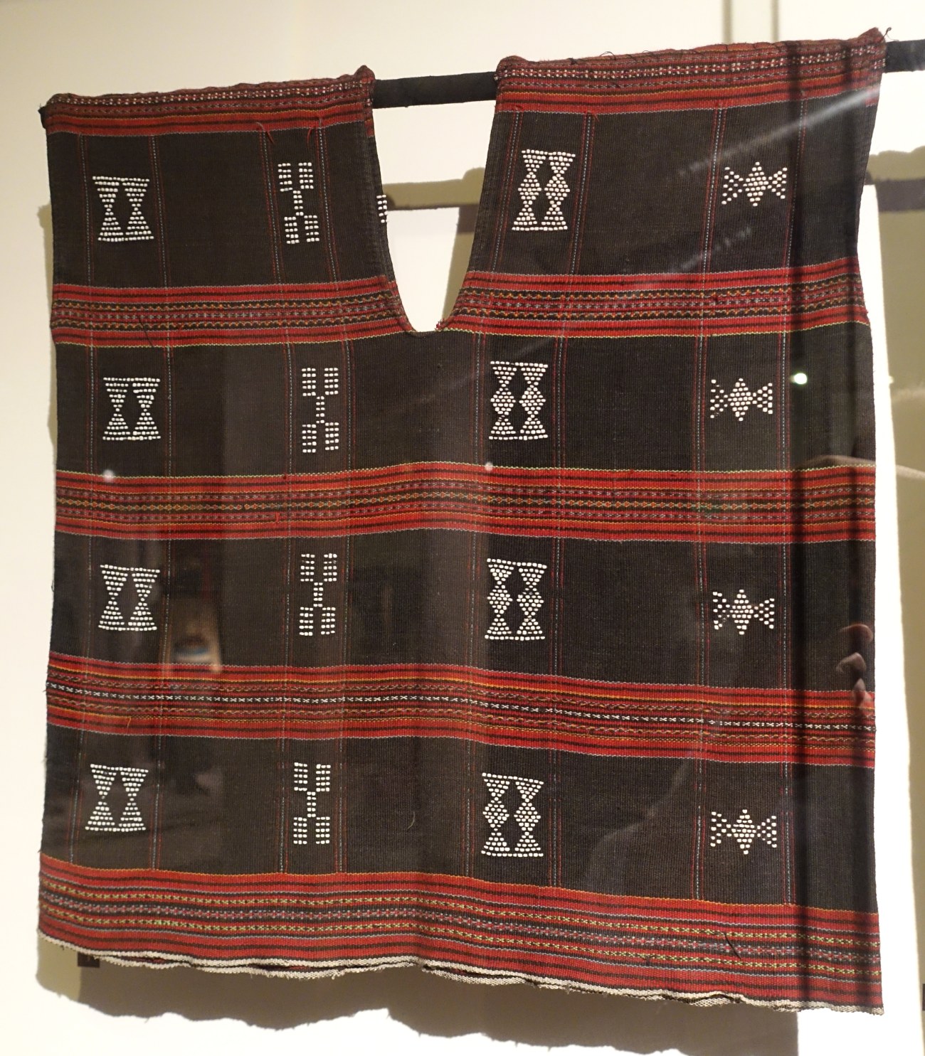 A dark woven vest patterned with rows of small white beads