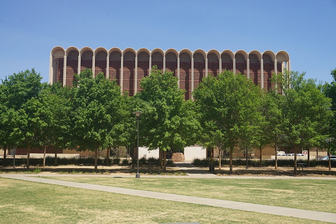 A long library building with a row of tall concrete fins, behind a line of trees