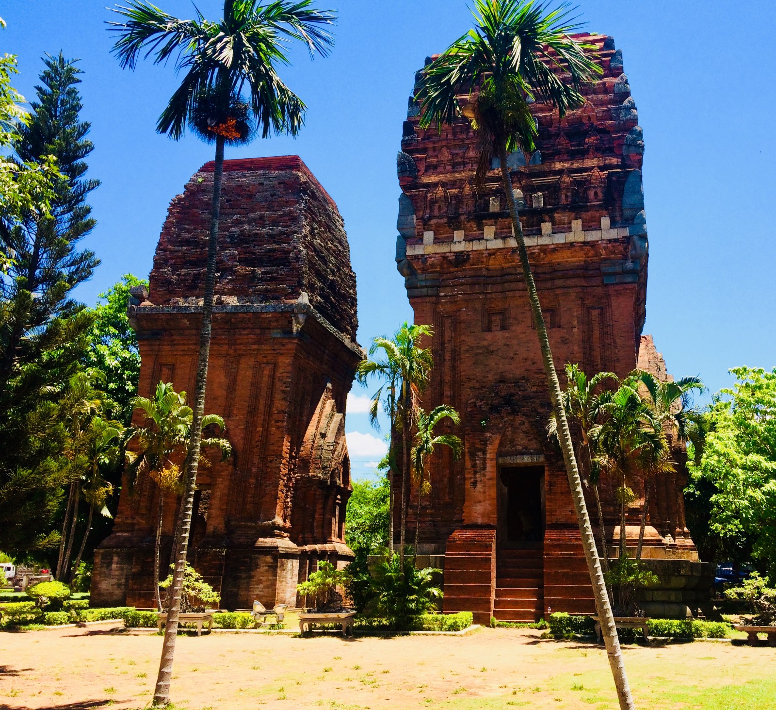 Two brick Cham towers side by side under trees