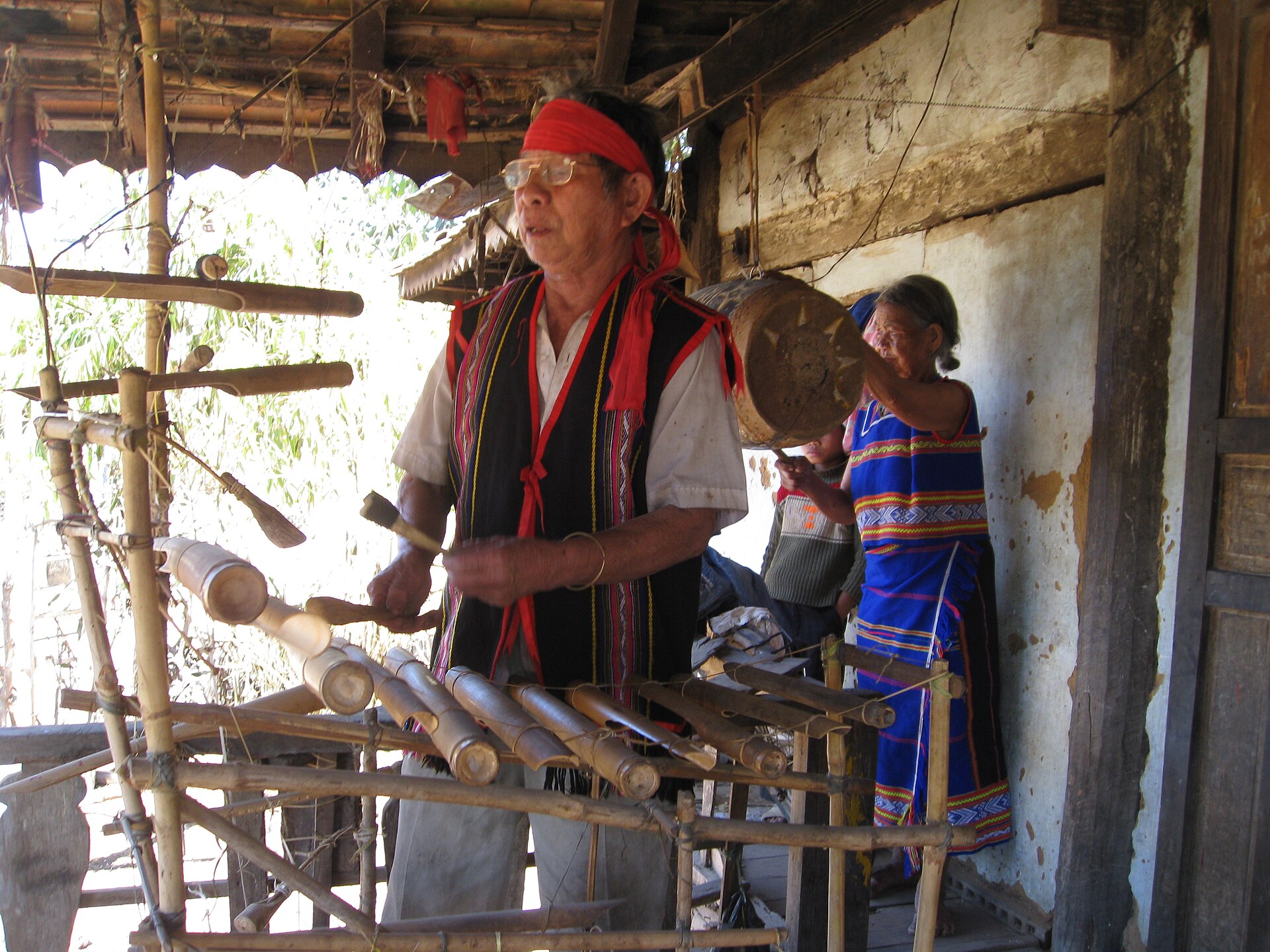 A man in a red headscarf playing a bamboo xylophone on a frame