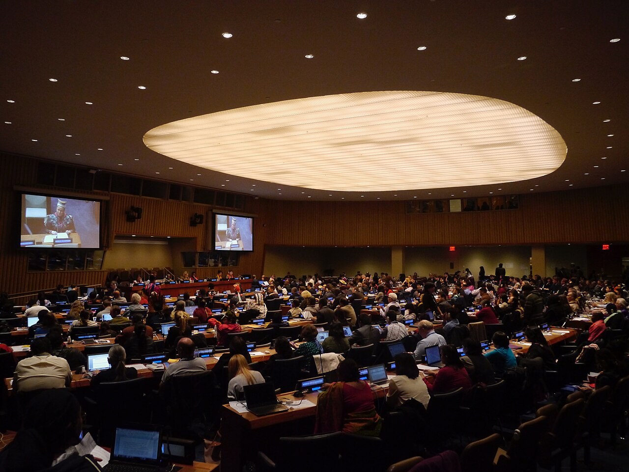 A large conference room at UN headquarters full of delegates at curved rows of desks, with screens at the front