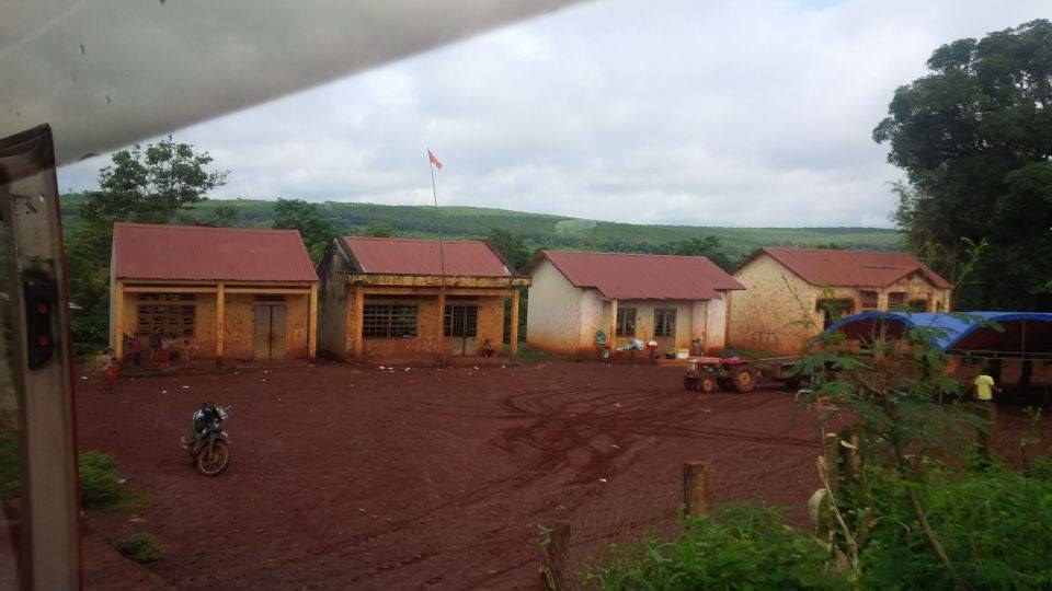 A row of low tile-roofed school buildings on bare red earth