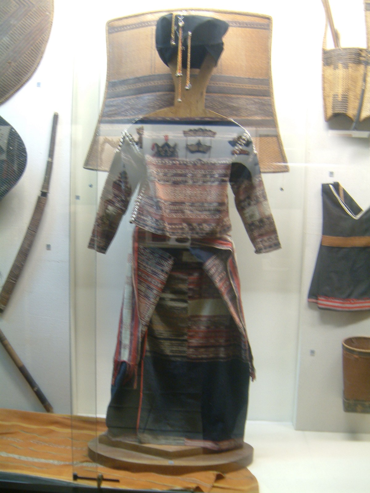 A mannequin in dark woven dress with red bands, in a museum