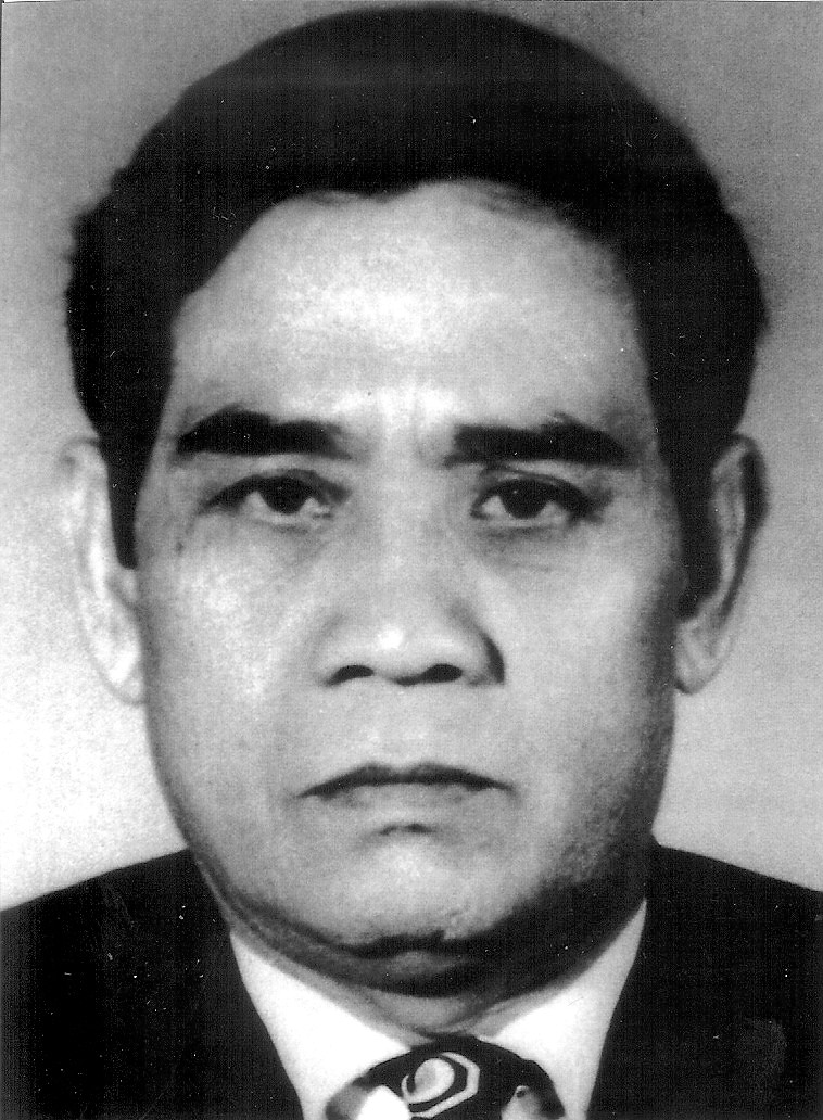 Y Bham Enuol in a dark suit and tie, a head-and-shoulders studio portrait