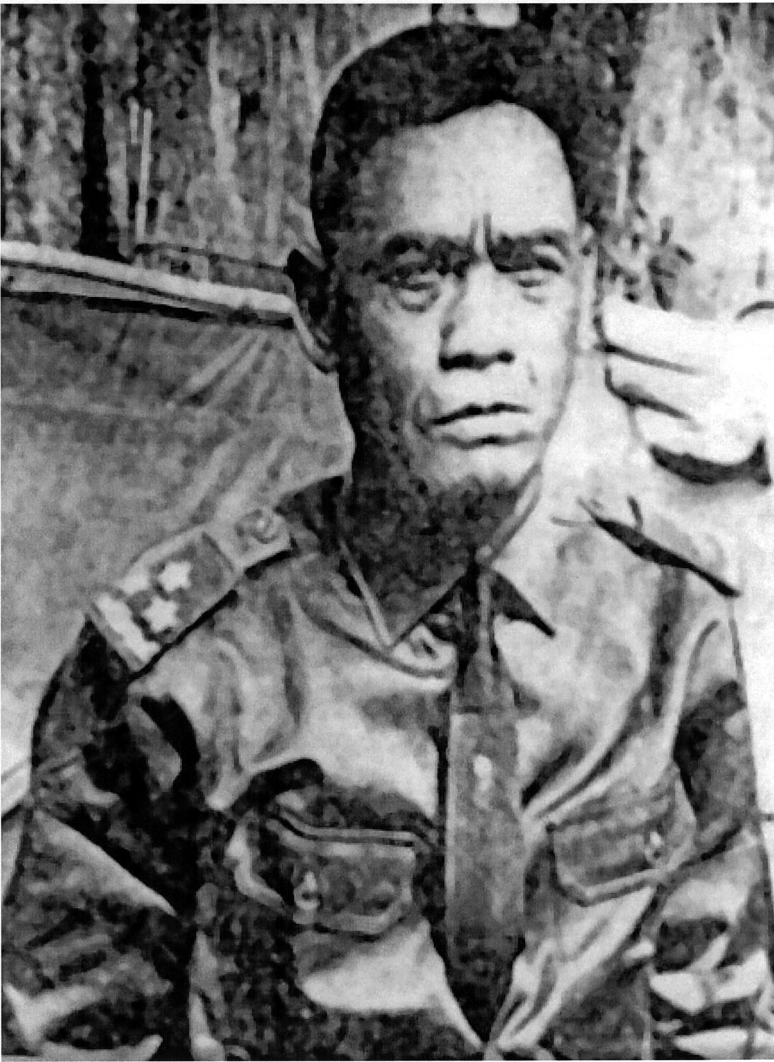 Y Bham Enuol seated in uniform with stars on the shoulder board, a camp behind him